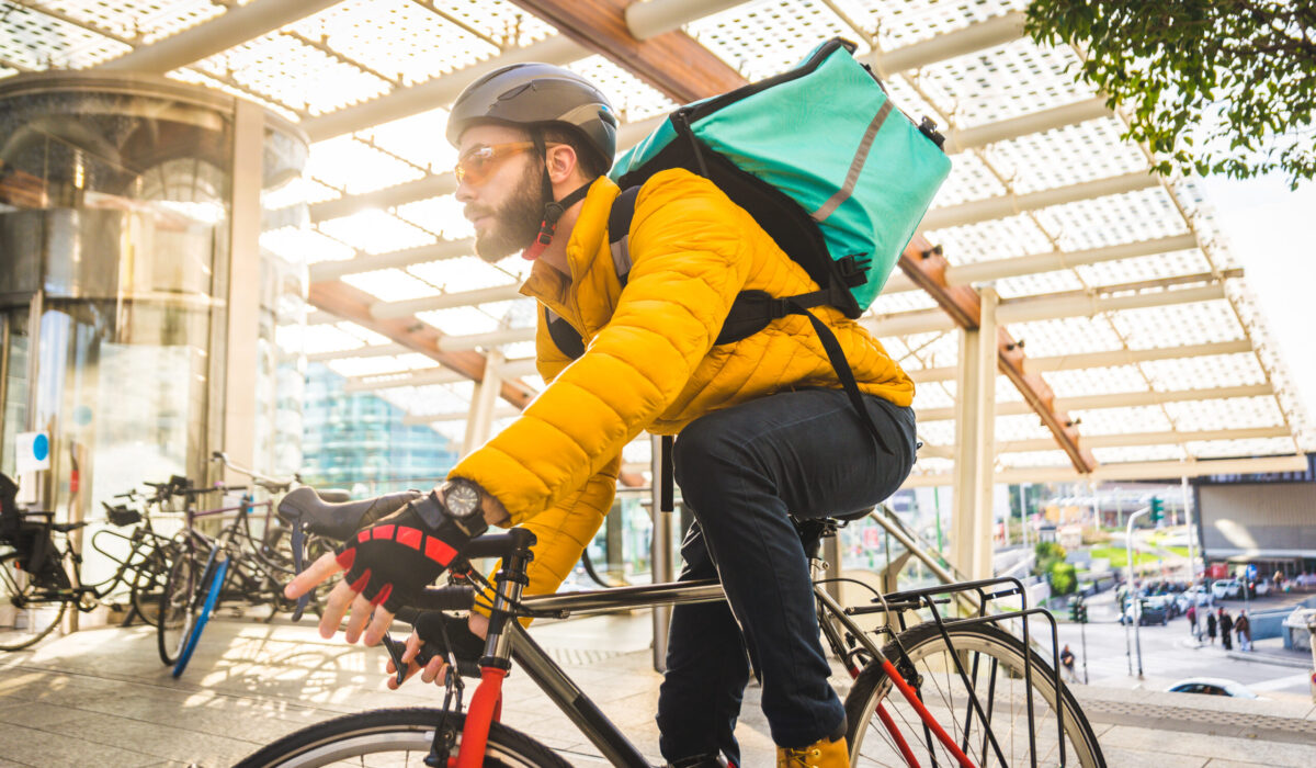 Fahrradkurier mit gelber Jacke und grünem Transportrucksack liefert Pakte mit dem Fahrrad an Kunden