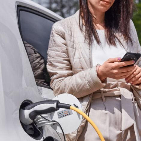 Frau schaut auf ihr Smartphone beim Laden eines E-Autos