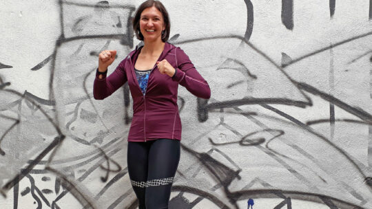 Mag. Sophie Wirth im Sportoutfit vor einer Graffiti Mauer