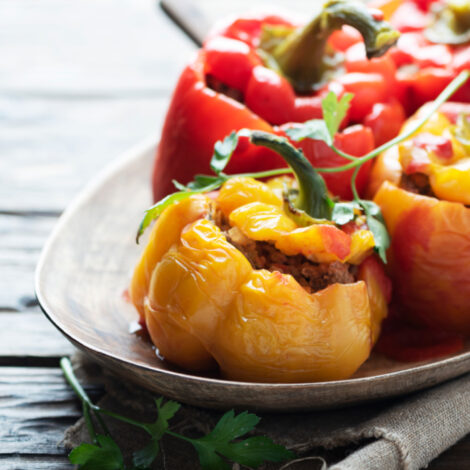 2 gelbe und 2 rote gefüllte und gegarte Paprika auf einem Teller mit Tomatensauce