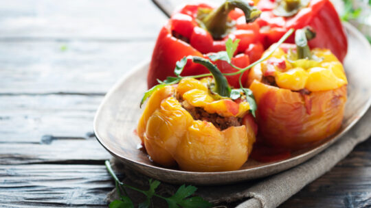 2 gelbe und 2 rote gefüllte und gegarte Paprika auf einem Teller mit Tomatensauce