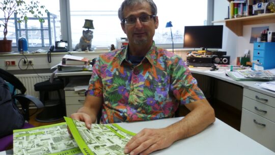 Dr. Hutter sitzt im seinem Büro am Besprechungstisch mit einer Broschüre in der Hand