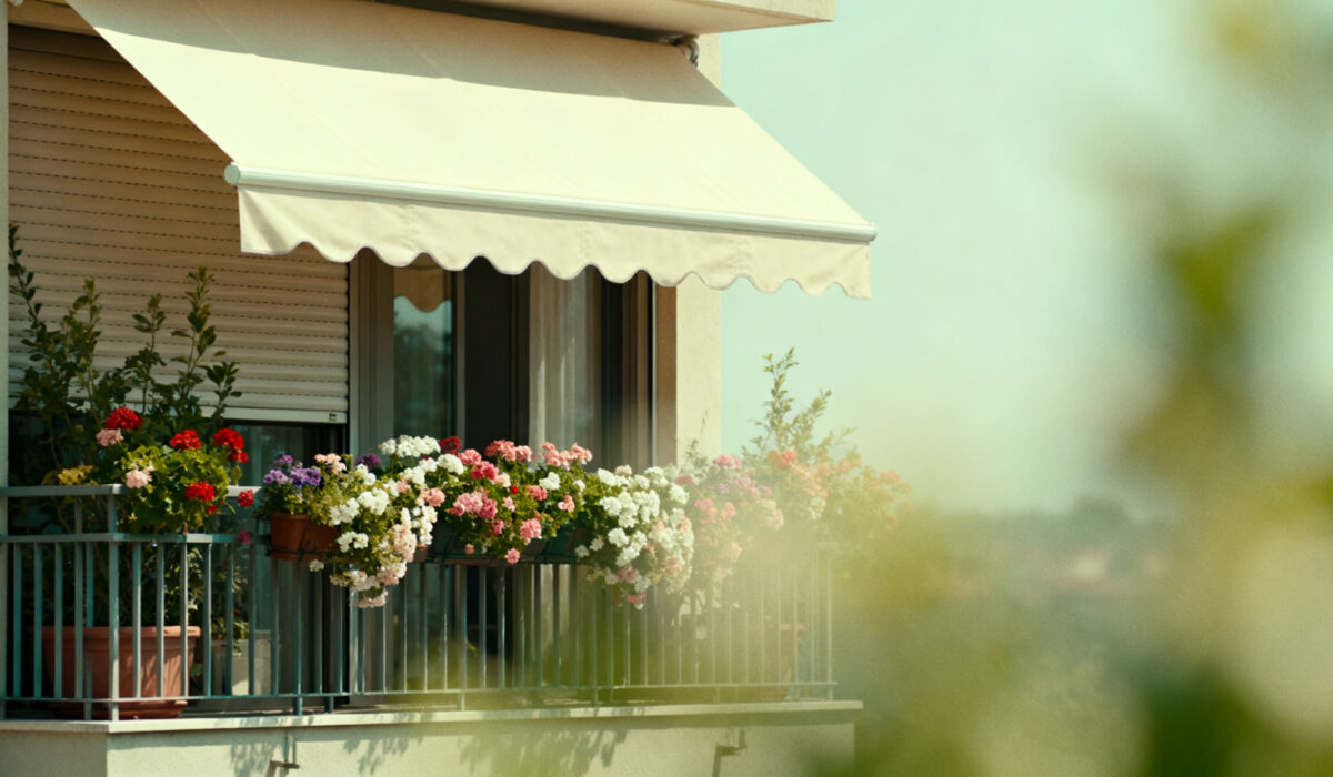 Foto, heißer Sommertag, Balkon mit Blumen und Markise und heruntergelassenen Außenrollos zur Abkühlung
