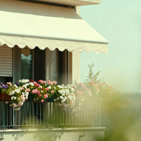 Foto, heißer Sommertag, Balkon mit Blumen und Markise und heruntergelassenen Außenrollos zur Abkühlung