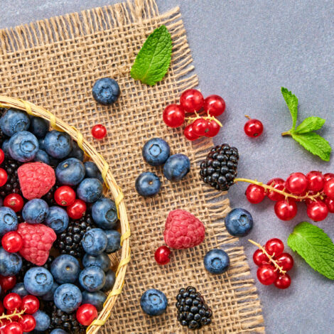 Verschiedene Beeren wie Himbeeren, Brombeeren, Heidelbeeren und Ribisel liegen in einer Holzschüssel und auf dem Tisch