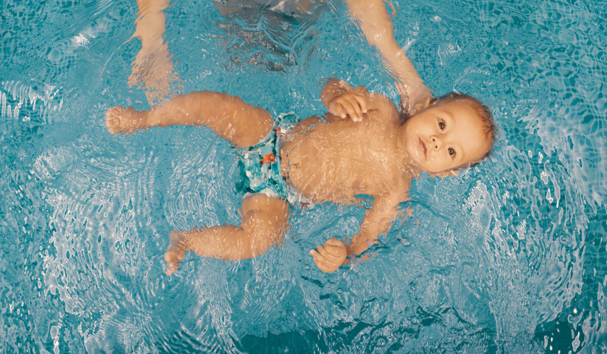 Baby mit Schwimmwindel wird von Mutter im Pool über Wasser gehalten