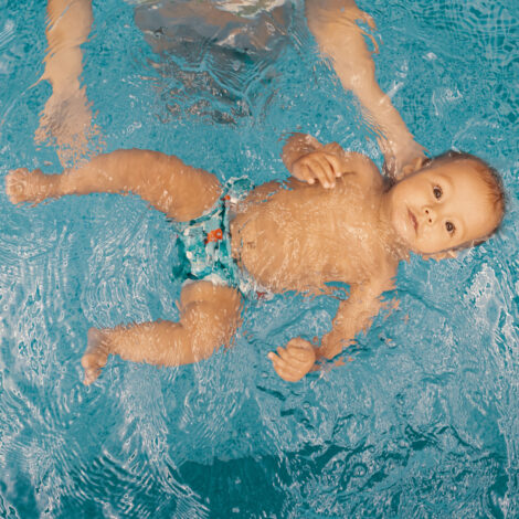 Baby mit Schwimmwindel wird von Mutter im Pool über Wasser gehalten