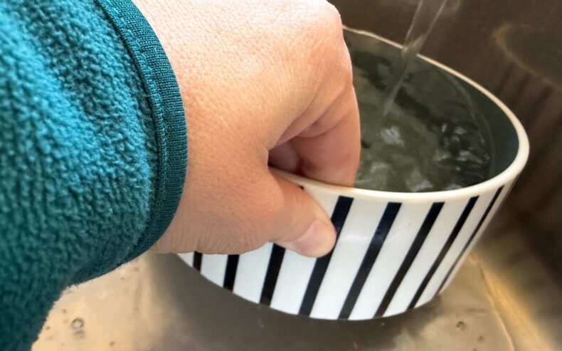 Hundefressnapf wird zur Reinigung unter laufendes Wasser im Waschbecken gehalten