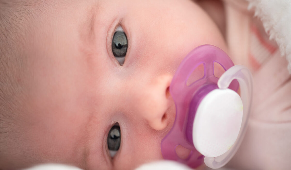 Neugeborenes Baby liegt auf der Seite mit einem rosa-weißen Schnuller im Mund