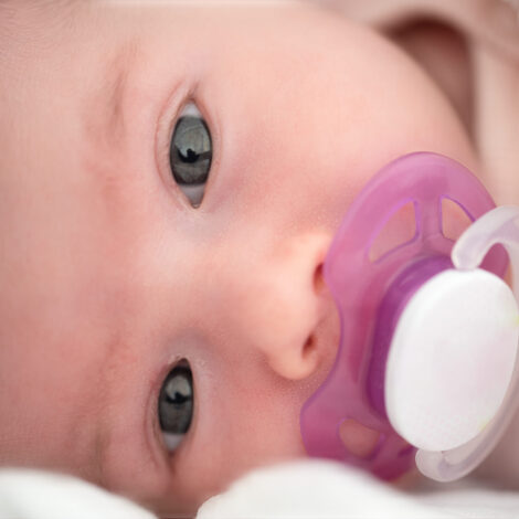 Neugeborenes Baby liegt auf der Seite mit einem rosa-weißen Schnuller im Mund