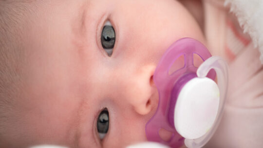 Neugeborenes Baby liegt auf der Seite mit einem rosa-weißen Schnuller im Mund