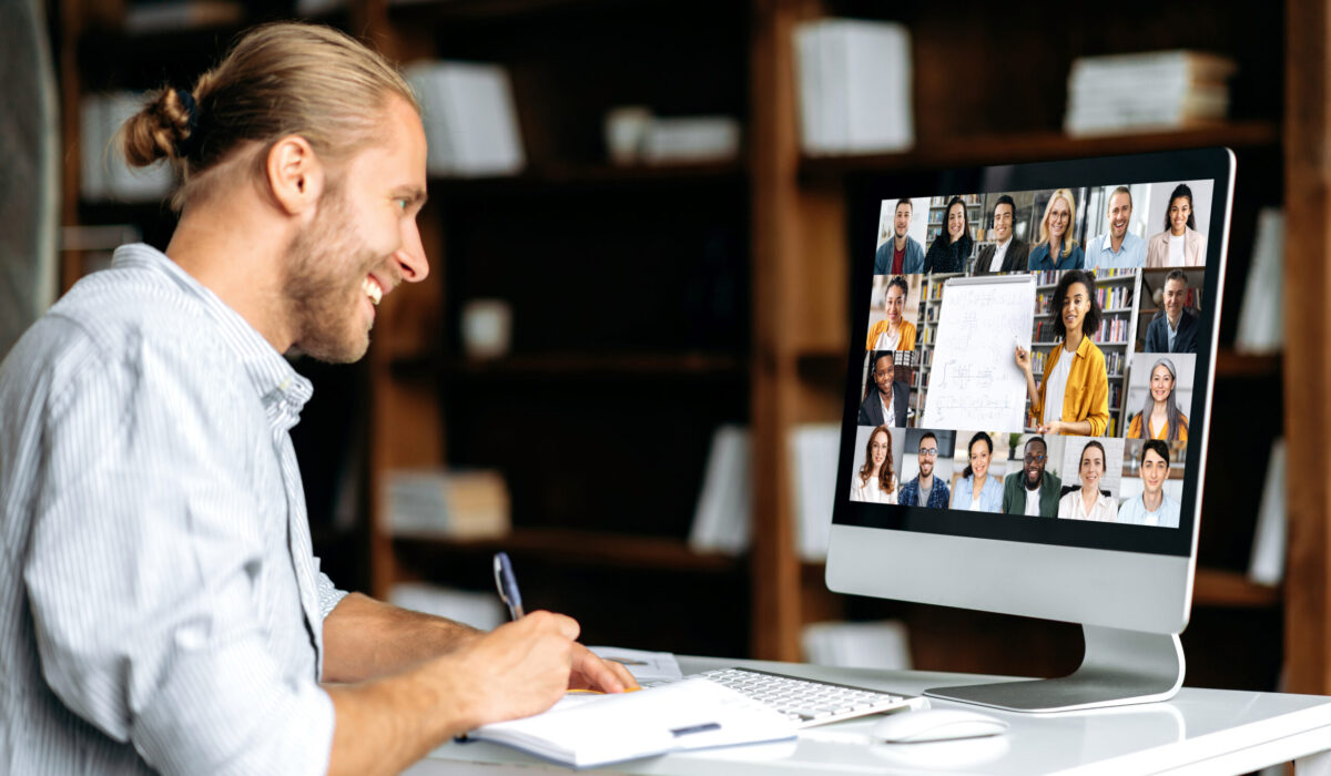 Junger Mann sitzt vor einem PC nimmt an einem online-Seminar teil und schreibt sich Informationen in ein Notizbuch