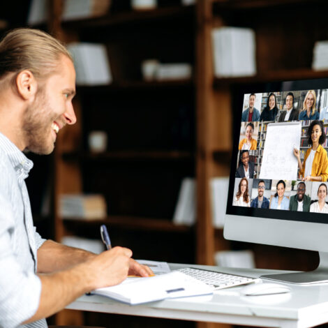 Junger Mann sitzt vor einem PC nimmt an einem online-Seminar teil und schreibt sich Informationen in ein Notizbuch