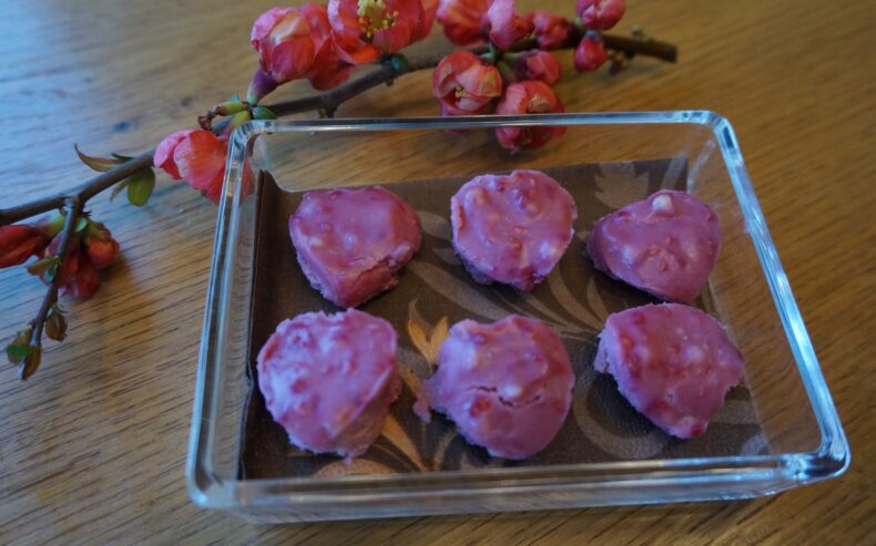 handgemachte herzförmige Pralinen in viereckiger Glasschüssel auf einem mit Blumen dekorierten Tisch