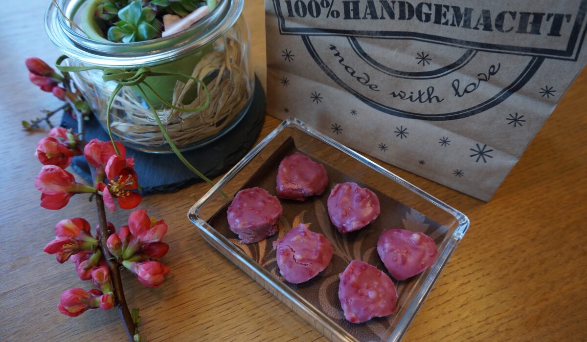 handgemachte herzförmige Pralinen in viereckiger Glasschüssel auf einem mit Blumen dekorierten Tisch