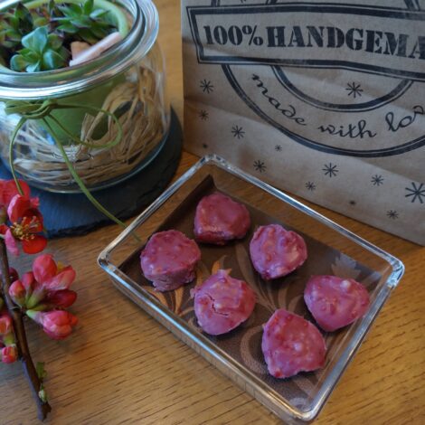 handgemachte herzförmige Pralinen in viereckiger Glasschüssel auf einem mit Blumen dekorierten Tisch