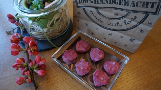 handgemachte herzförmige Pralinen in viereckiger Glasschüssel auf einem mit Blumen dekorierten Tisch