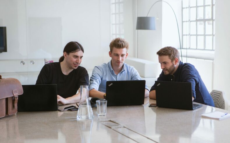 Die drei Gründer von refurbed sitzen rund um eine Laptop und besprechen