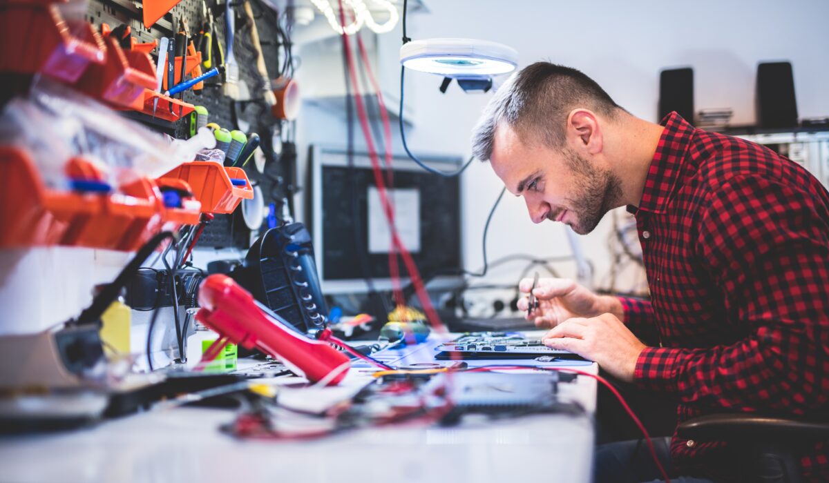 Mann sitzt an Werkbank und repariert ein Elektrogerät