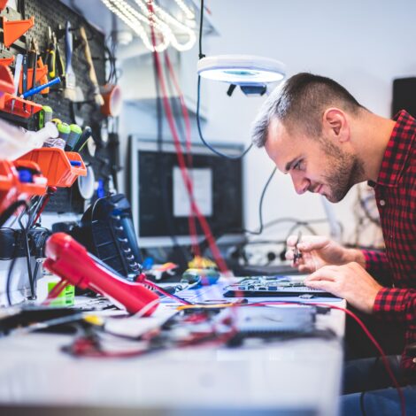 Mann sitzt an Werkbank und repariert ein Elektrogerät