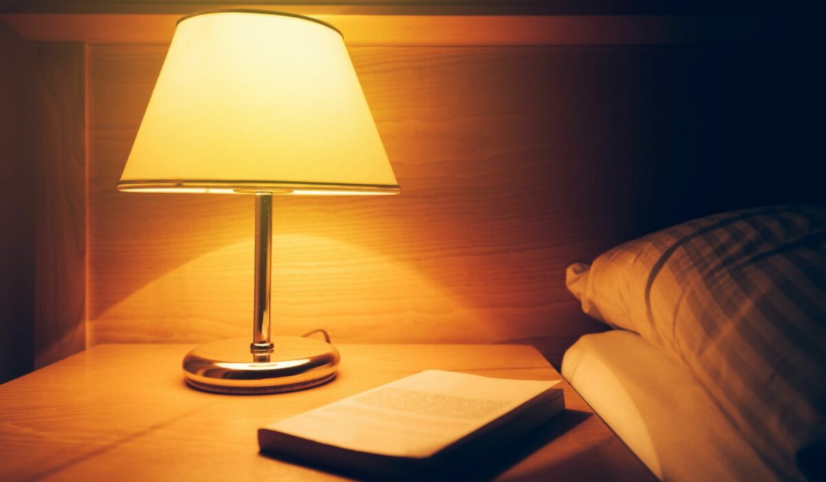 Nachttischlampe mit warmem Licht und Buch am Nachttisch