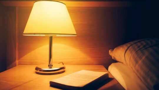 Nachttischlampe mit warmem Licht und Buch am Nachttisch