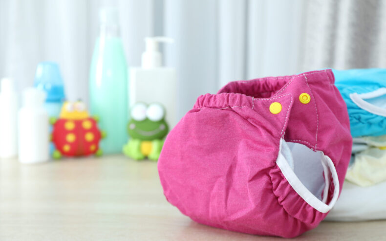 Pinke Stoffwindel mit gelben Druckknöpfen mit unscharfen Windeln und Cremen im Hintergrund