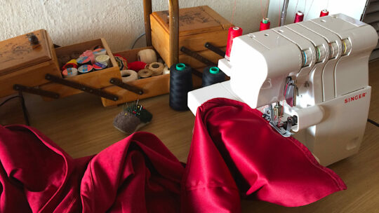 Nähmaschine mit rotem Seidenstoff und Nähkästchen auf Holztisch