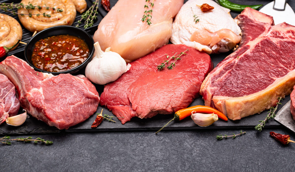 Fleischprodukte wie rohes Rindfleisch, Hühnerfleisch, Würste auf einer Schieferplatte aufgelegt