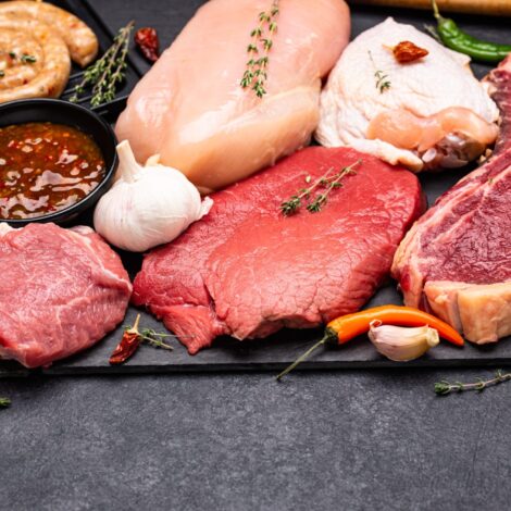 Fleischprodukte wie rohes Rindfleisch, Hühnerfleisch, Würste auf einer Schieferplatte aufgelegt