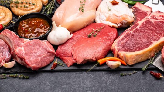 Fleischprodukte wie rohes Rindfleisch, Hühnerfleisch, Würste auf einer Schieferplatte aufgelegt