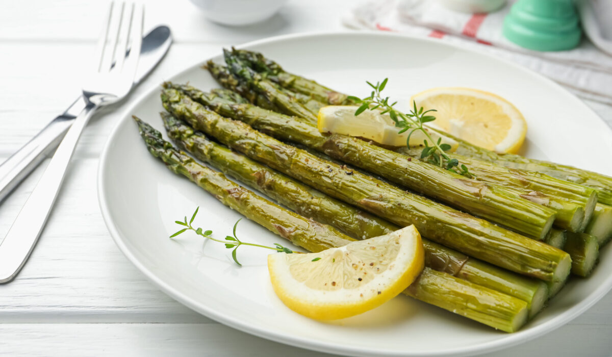 In Bärlauchbutter beratener Bund grüner Spargel auf einem Teller mit Zitronen und Thymian dekoriert