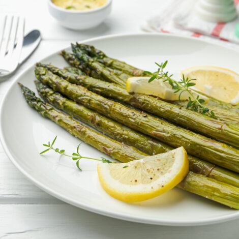 In Bärlauchbutter beratener Bund grüner Spargel auf einem Teller mit Zitronen und Thymian dekoriert