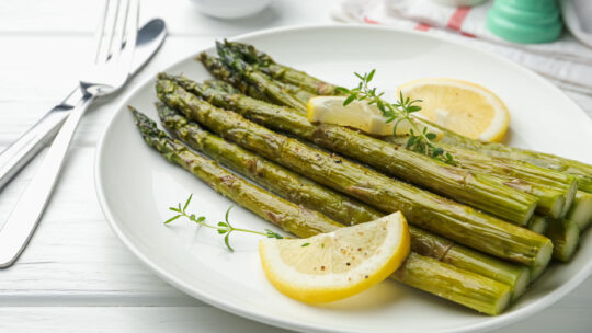 In Bärlauchbutter beratener Bund grüner Spargel auf einem Teller mit Zitronen und Thymian dekoriert
