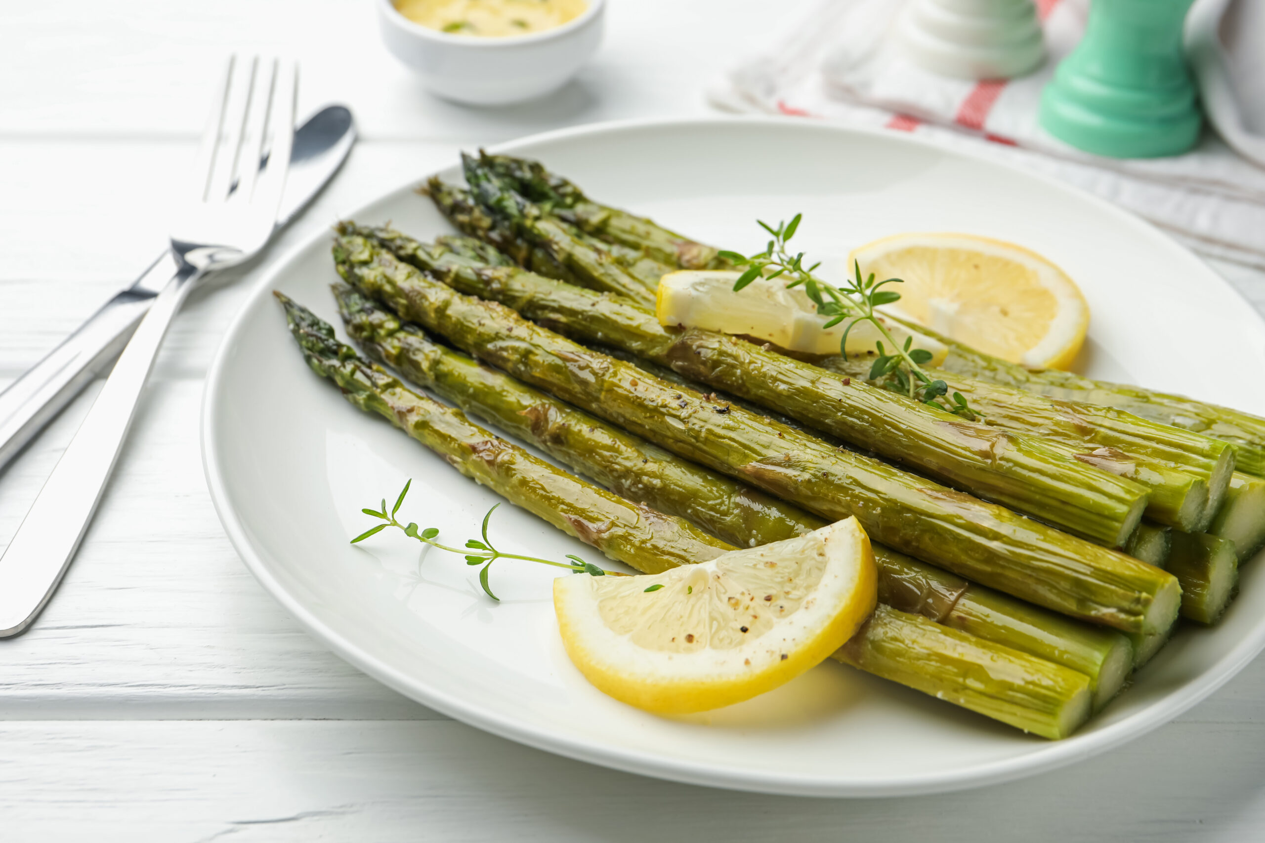 In Bärlauchbutter beratener Bund grüner Spargel auf einem Teller mit Zitronen und Thymian dekoriert