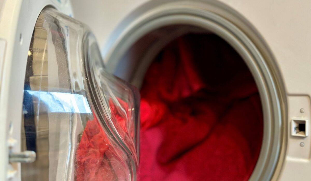 Offene Waschmaschine voll gefüllt mit bunten, roten Handtüchern und T-Shirts