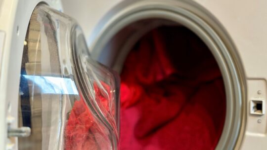 Offene Waschmaschine voll gefüllt mit bunten, roten Handtüchern und T-Shirts