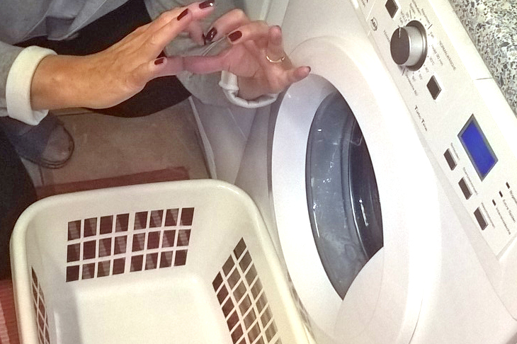 Mit Händen geformtes Herz vor der offenen Waschmaschine mit Wäschekorb