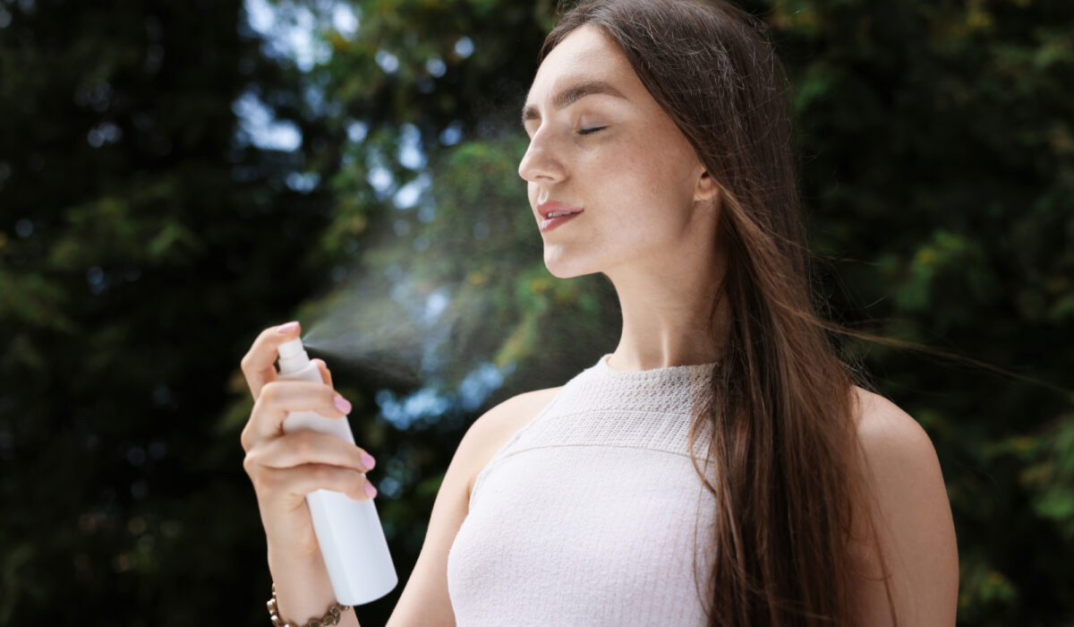 Junge Frau sprüht sich mit einem Wasserspray erfrischendes Wasser ins Gesicht