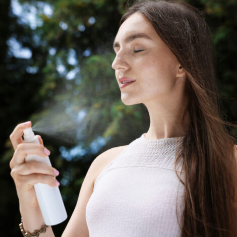 Junge Frau sprüht sich mit einem Wasserspray erfrischendes Wasser ins Gesicht