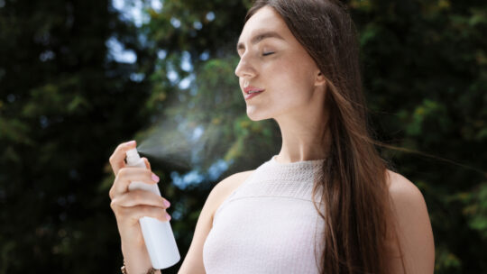 Junge Frau sprüht sich mit einem Wasserspray erfrischendes Wasser ins Gesicht