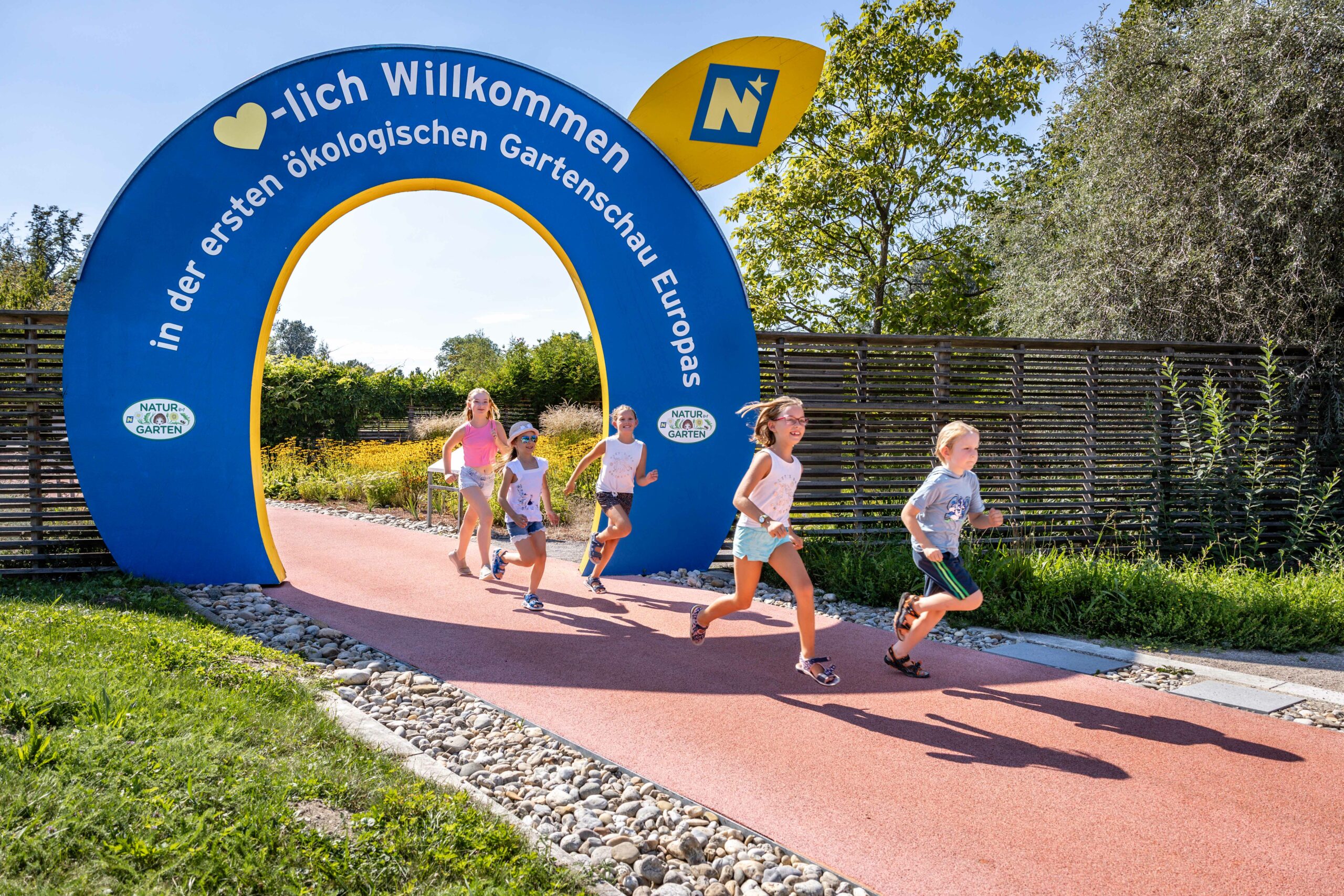 Kinder laufen durch einen Herzlich Willkommen Bogen der Garten Tulln auf einem Weg