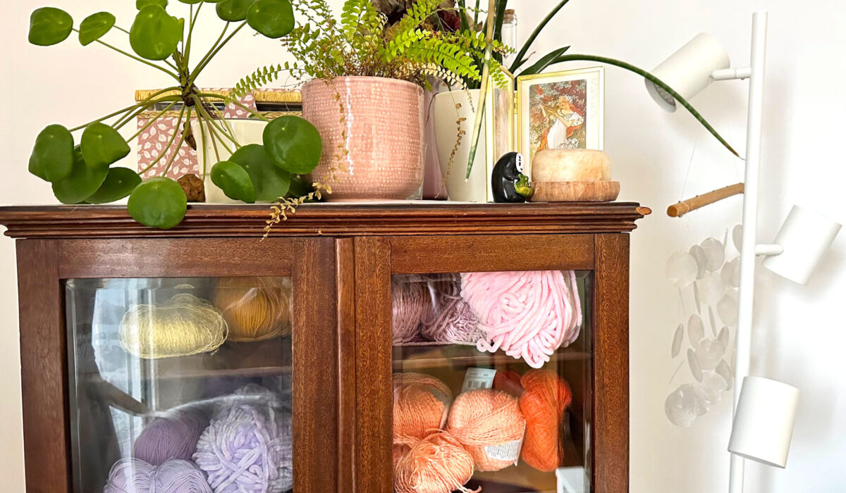 Alte Glasvitrine mit Topfpflanzen mit vielen bunten Wollknäuel zum Stricken drinnen
