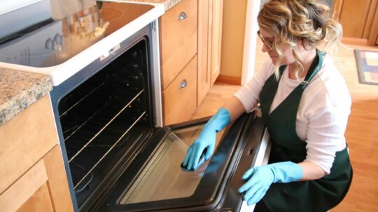 Frau reinigt den Backofen mit Gummihandschuhen une einem Schwämmchen.