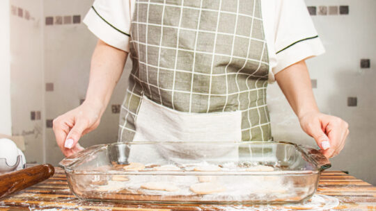Frau in Schürze hält ein Glas Backblech mit Keksen in den Händen