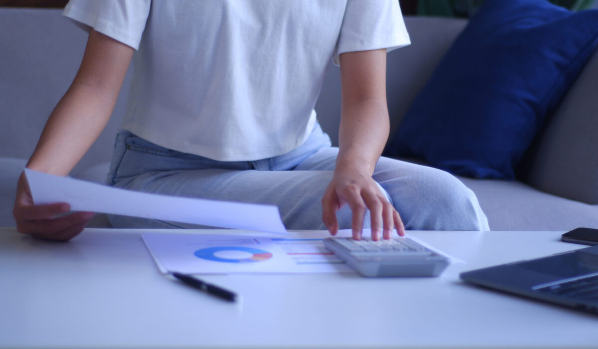 Junge Frauen arbeiten von zu Hause aus und analysieren Daten mit Taschenrechner und Laptop.
