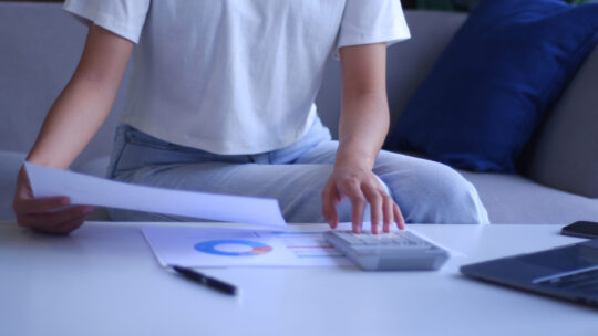 Junge Frauen arbeiten von zu Hause aus und analysieren Daten mit Taschenrechner und Laptop.